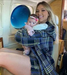 a woman holding a baby wrapped in a blue plaid blanket while sitting on an airplane