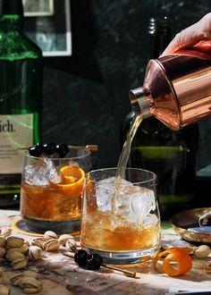 a person pouring an alcoholic drink into a glass filled with ice and orange peels