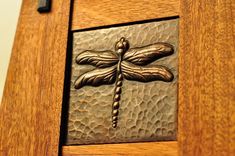 a close up of a dragonfly on a wooden door with metal detail inlays