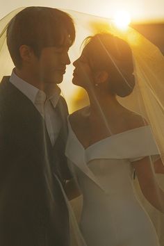 a bride and groom standing under a veil in front of the sun at their wedding