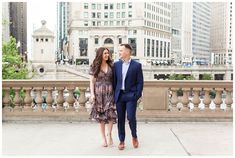 a man and woman standing next to each other in front of tall buildings on a bridge