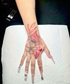 a woman's hand painted with red and pink flowers on her left palm, while she is sitting on a white sheet