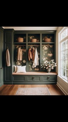 a room with green cabinets and flowers on the wall, two coats hanging from hooks