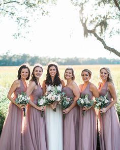 a group of women standing next to each other in front of a lush green field