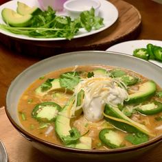 two bowls filled with soup and vegetables on top of a wooden table next to green peppers