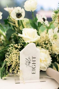 white flowers and greenery are arranged on a table