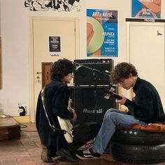 two young men sitting on top of an old tire in a music studio playing instruments