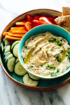 a bowl filled with hummus, cucumbers, carrots and crackers