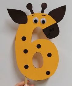 a child's hand holding up a yellow and black paper number six with a ladybug on it