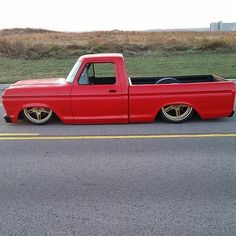 a red pick up truck parked on the side of the road with grass in the background