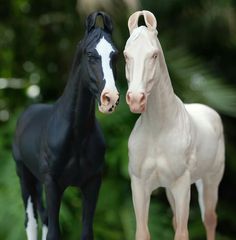 two toy horses standing next to each other on a table with trees in the background