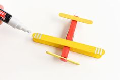 a hand holding a marker next to a model airplane on a white surface with red and yellow strips