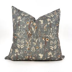 a blue pillow with white and brown flowers on the front, sitting on a white surface