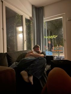 a man sitting on top of a couch in front of a window next to a plant