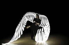 a woman sitting on the ground with an angel wing in front of her, lit up at night