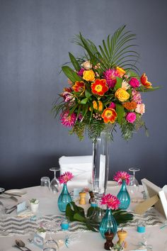 a vase filled with lots of colorful flowers on top of a white table cloth covered table