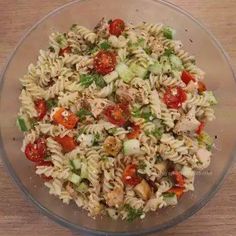 a glass bowl filled with pasta salad on top of a wooden table