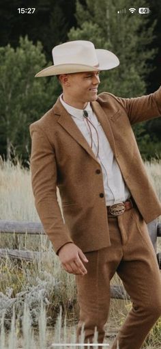 a man in a brown suit and hat standing next to a fence with his hand on his hip