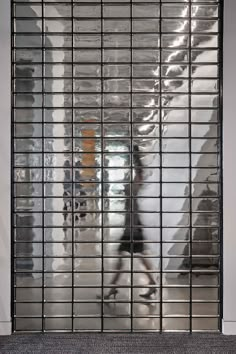 the reflection of a man riding a skateboard through a metal gate in an office building