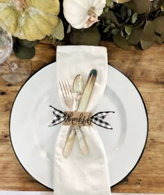 a place setting with silverware, napkins and pumpkins on a wooden table