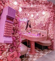 a woman sitting at a pink table in a room with flowers on the walls and floor