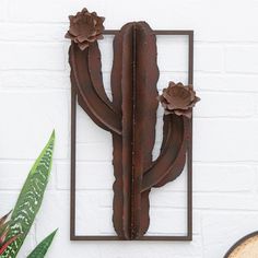 a metal cactus is mounted to the side of a white brick wall next to a potted plant