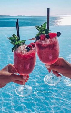 two people holding up wine glasses with fruit in them near the water and blue sky