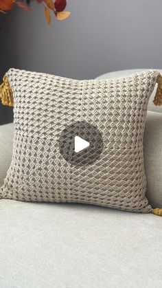 a knitted pillow with a play button on it sitting on a couch in front of a plant