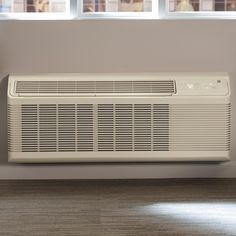 a white air conditioner sitting on top of a wooden floor next to two windows