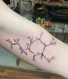 a branch tattoo on the left arm with leaves and branches in black ink, sitting on top of a wooden table