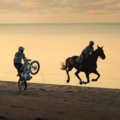 two people are riding horses on the beach at sunset, one is jumping over the other