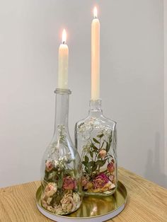 two glass vases with flowers and candles on a wooden table next to each other