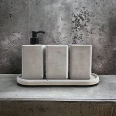 three soap dispensers sitting on top of a metal tray next to a concrete wall