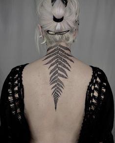 the back of a woman's neck with a fern tattoo on it