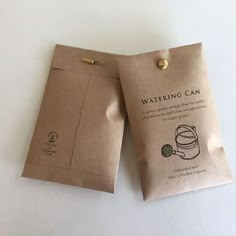 two brown paper bags sitting next to each other on a white counter top, one has a clip in it and the other has a button that says watering can