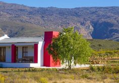 a red and white house sitting in the middle of a field with mountains in the background