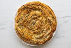 a white plate topped with a pastry on top of a marble countertop next to a knife and fork