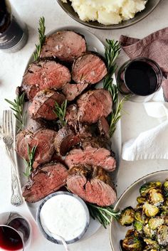 meat and vegetables on a platter with sauces next to the plate full of potatoes