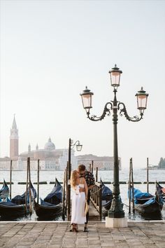 a couple kissing in front of some gondolas on the water near a street light