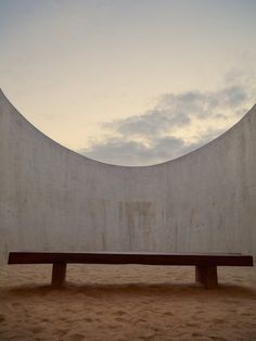 a wooden bench sitting in front of a concrete wall on the beach at sunset or dawn