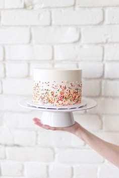 a person holding a cake with sprinkles on it in front of a brick wall