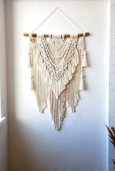 a white wall hanging with some tassels on it's sides and a plant in the corner