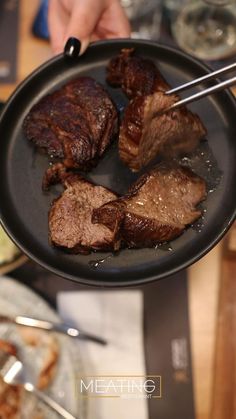 a person holding a plate with steak on it and tongs in the other hand