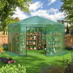 a green house in the middle of a yard with a lawn mower parked next to it