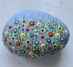 a painted rock sitting on top of a white surface with grass and flowers all over it