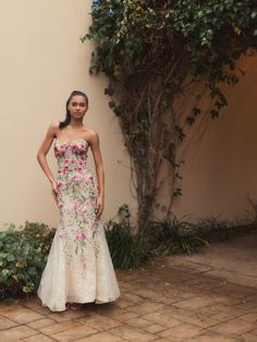 a woman standing in front of a wall wearing a dress with pink flowers on it