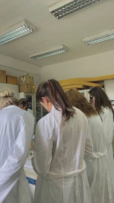 three women in white lab coats are looking at something on the counter and taking pictures