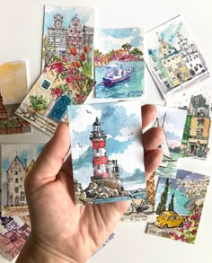 a person holding up some cards in their hand with watercolors on them and buildings