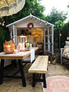 a wooden table sitting on top of a wooden floor next to a white shed with lights hanging from it's roof