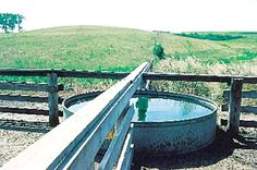 a large metal barrel sitting on top of a wooden rail next to a field with green grass